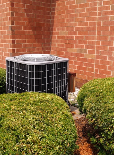 Air conditioner with brick building in background. Transitioning Your Heat Pump.