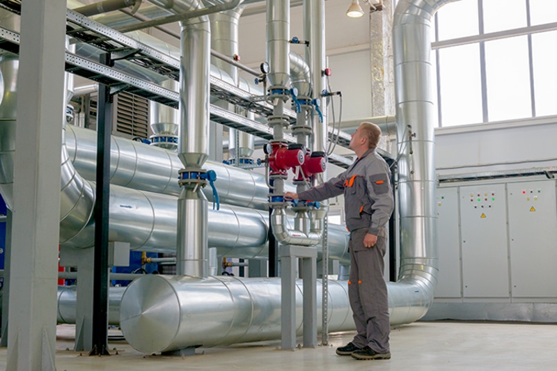 Commercial Heating Solutions. Image is a photograph of an HVAC professional working on commercial heating ductwork.